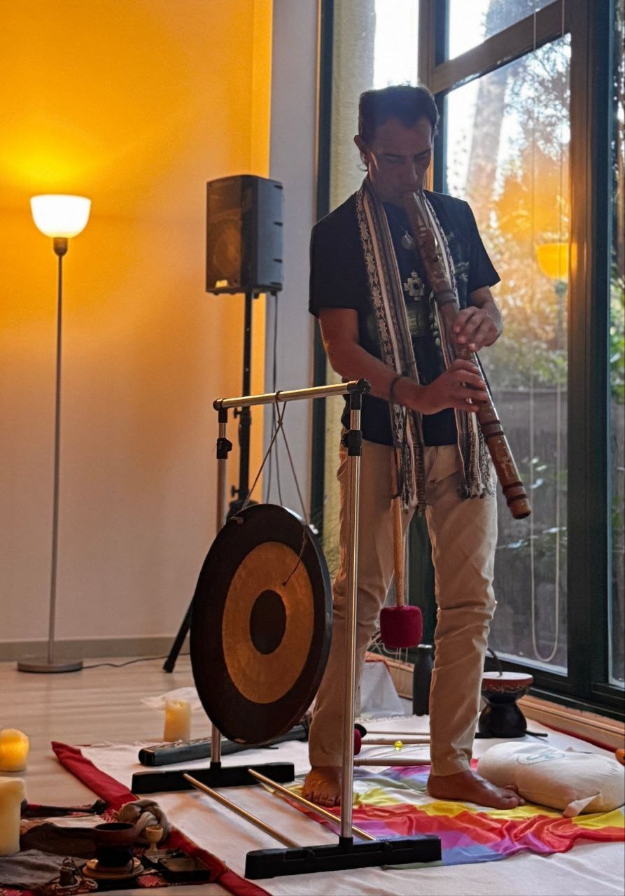 Músico de pie tocando una flauta junto a un gong, una lámpara y una ventana