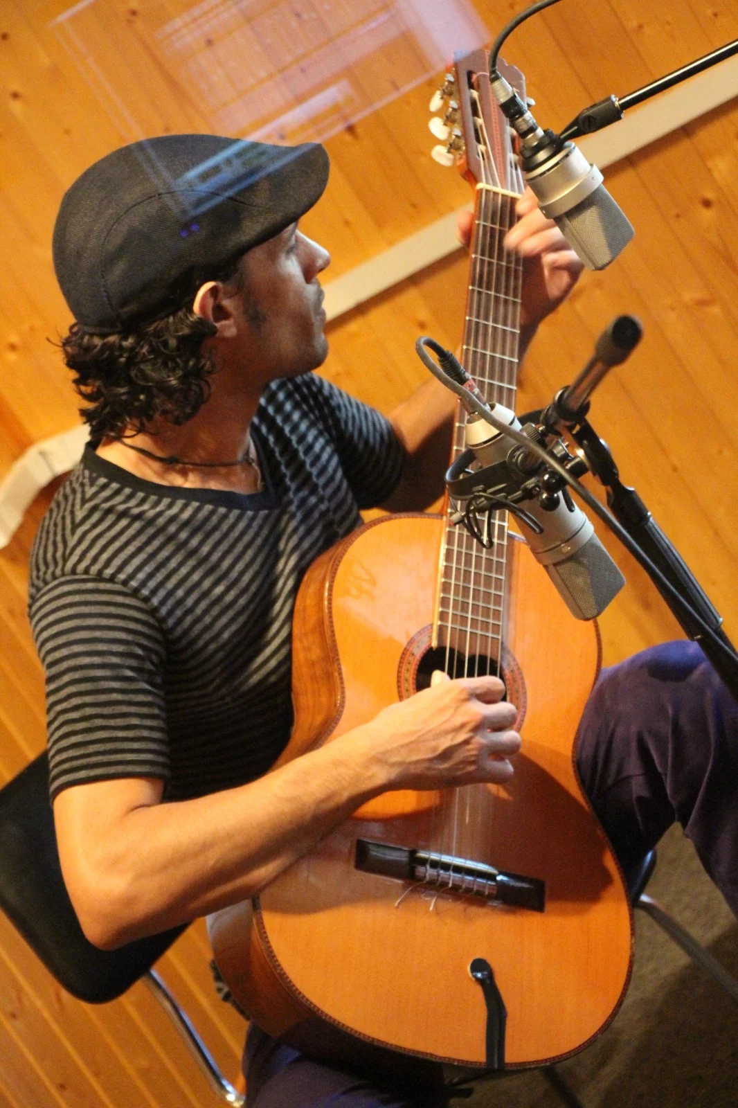 Músico sentado tocando una guitarra acústica frente a varios micrófonos